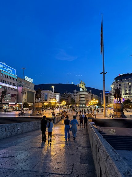 People walk across the Stone Bridge toward Macedonia Square at dusk in Skopje.
