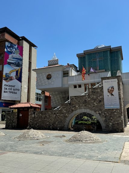 A stone gate building with posters stands on a paved square in Skopje.