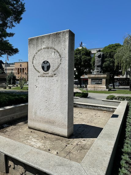 A tall stone memorial block stands in a square planter in central Skopje.