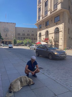 A traveler crouches next to a sleeping stray dog on a street in Skopje.