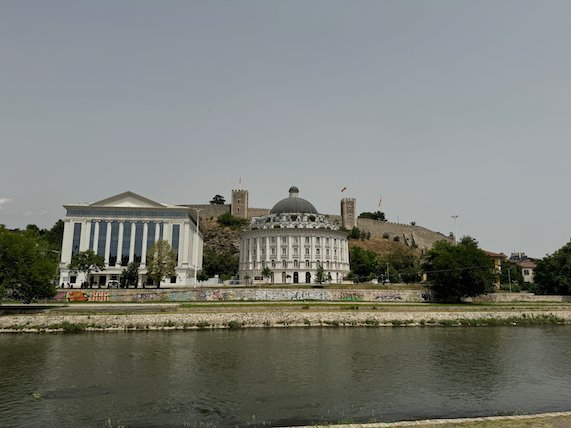 White neoclassical buildings and Kale Fortress stand above the Vardar River in Skopje.