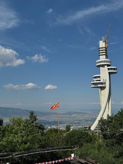 A tall white tower and a Macedonian flag stand above the city on Mount Vodno near Skopje.