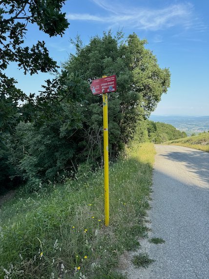 A yellow trail sign stands beside a mountain road with a view on Mount Vodno near Skopje.