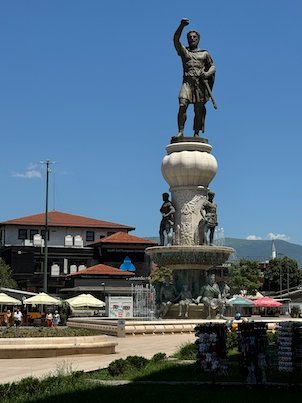 A warrior statue fountain stands in front of red roofs near the Old Bazaar in Skopje.