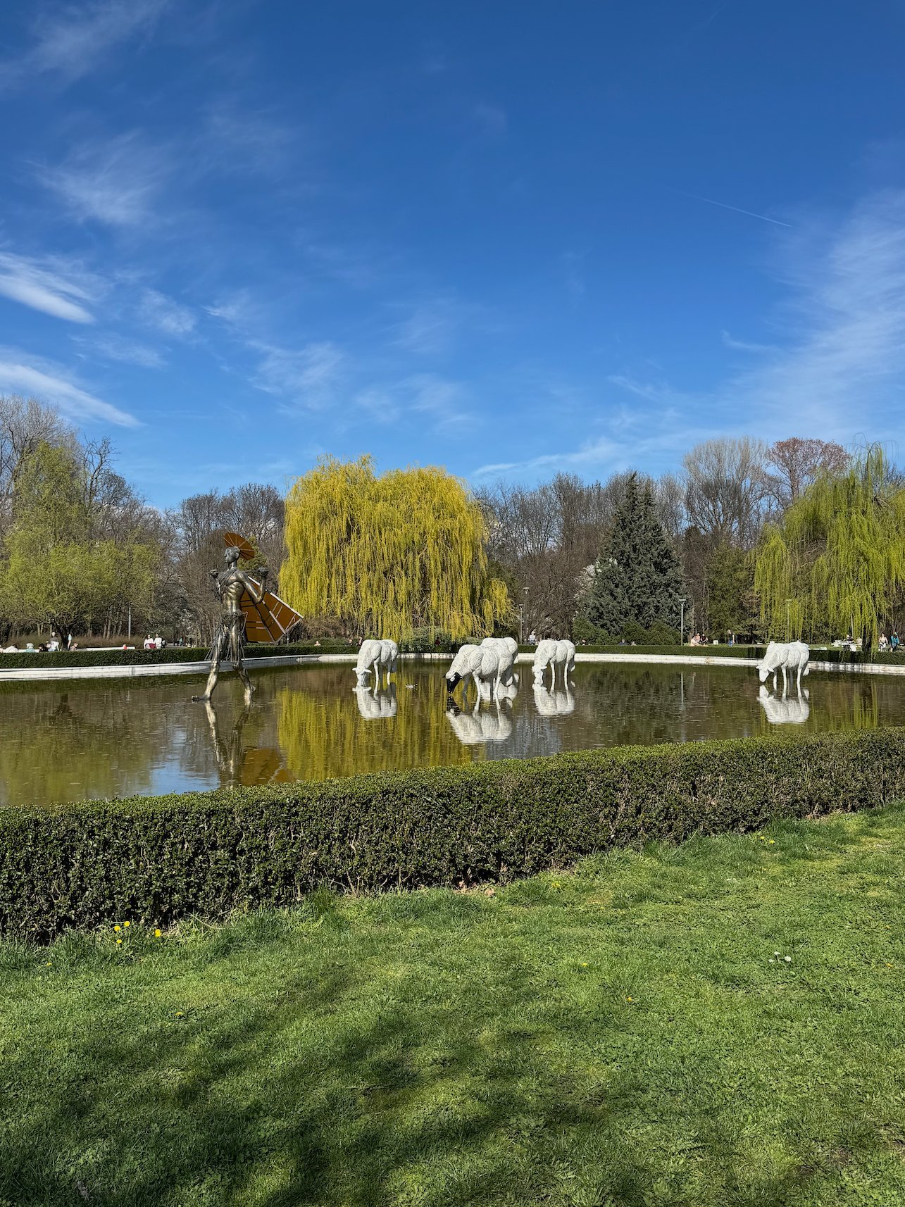 White horse sculptures stand at the edge of a pond with willow trees in Borisova Gradina park in Sofia.