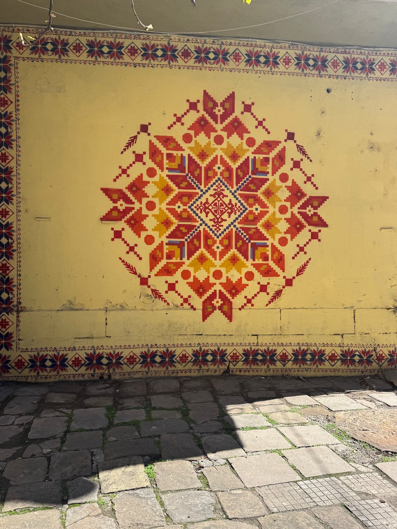 A red and orange folk embroidery pattern is painted on a yellow wall in Sofia.