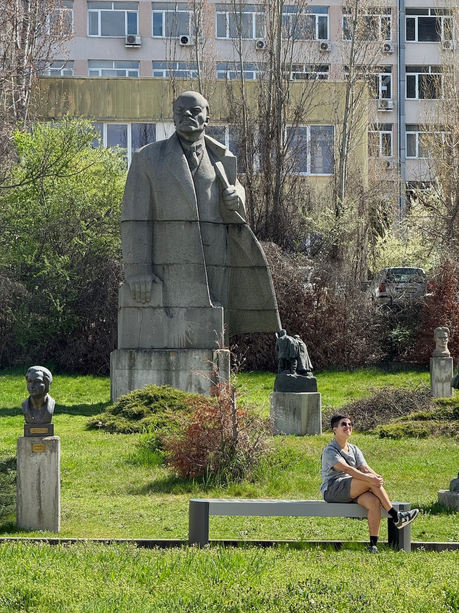 A traveler sits on a bench below a Lenin statue at the Museum of Socialist Art in Sofia.