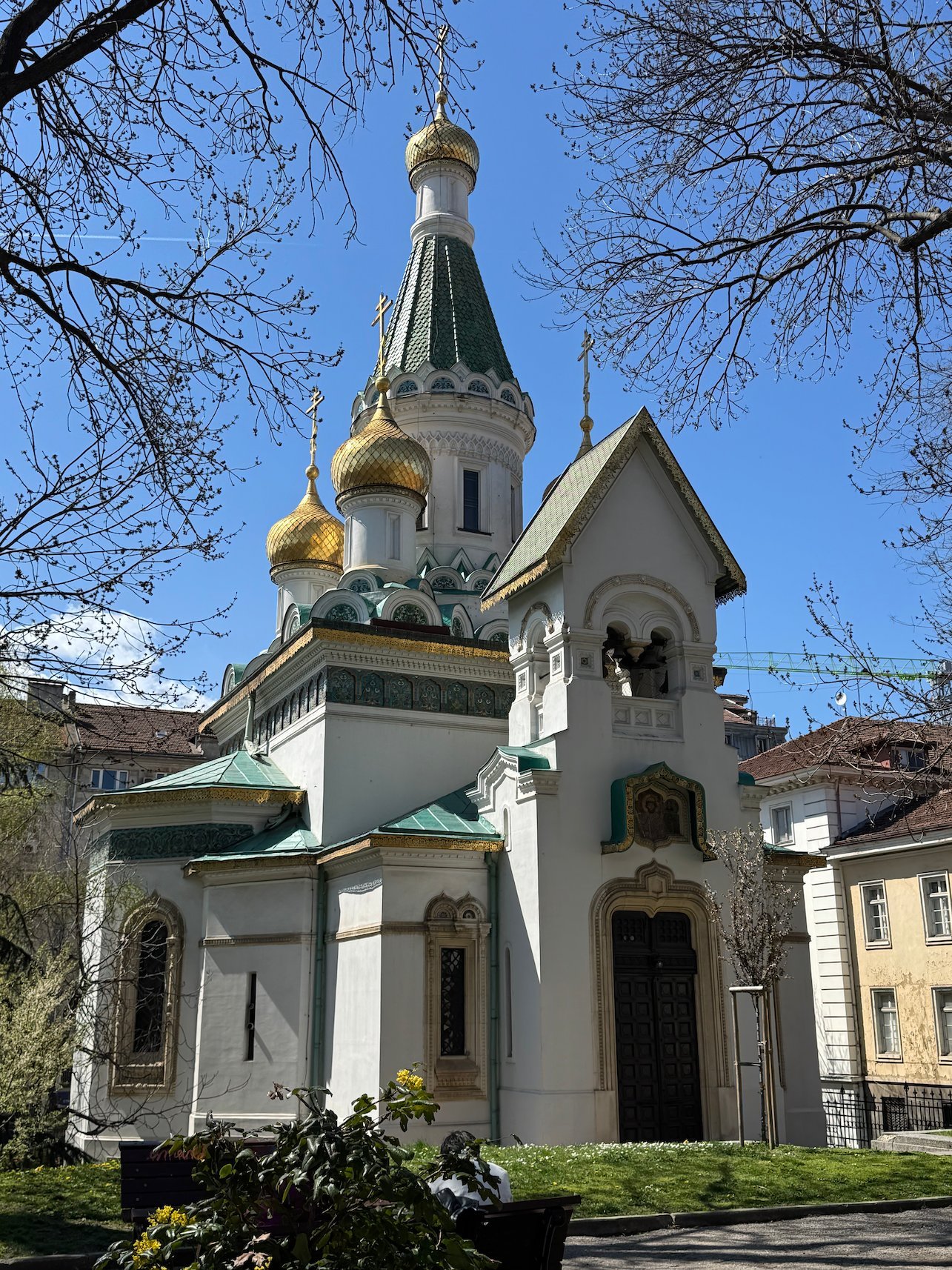 The Russian Church of St. Nicholas with golden onion domes stands among trees in Sofia.
