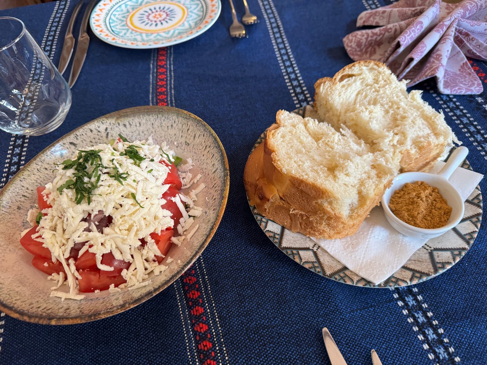 A shopska salad with white cheese and a plate of bread sit on a blue tablecloth in Sofia.