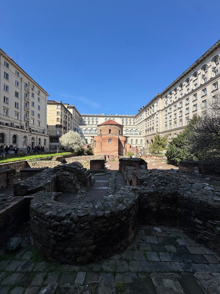 The red brick St. George Rotunda stands among Roman ruins and large government buildings in Sofia.