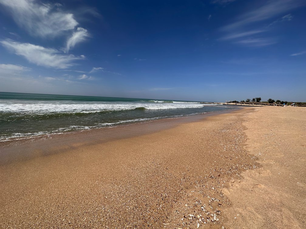 Waves roll onto a long sandy beach under a blue sky near Somone.
