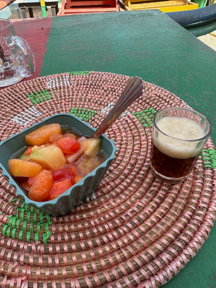 A bowl of fruit salad and a drink stand on a green table in Somone.
