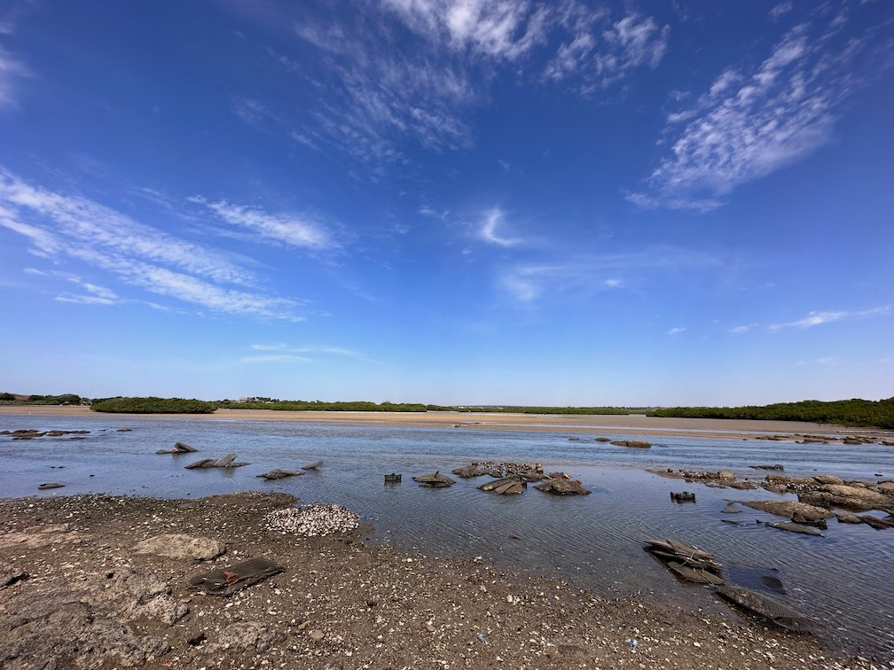 Rocks lie in shallow water under white clouds at the Somone lagoon.