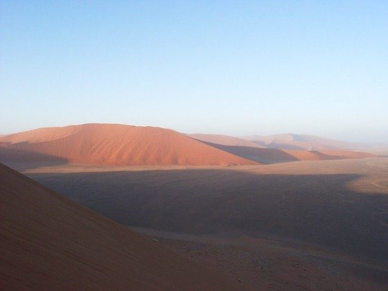 A big red dune rises over a valley in deep shadow at Sossusvlei, Namibia.