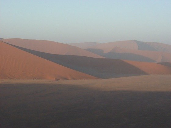Red sand dunes catch the first sunlight over a flat valley at Sossusvlei, Namibia.