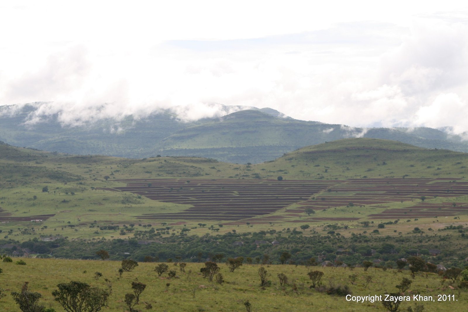 Green hills and farmland stretch below low clouds in the countryside of South Africa.