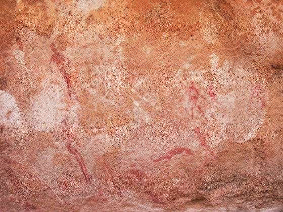 Red painted human figures and animals cover an orange rock wall at Spitzkoppe, Namibia.