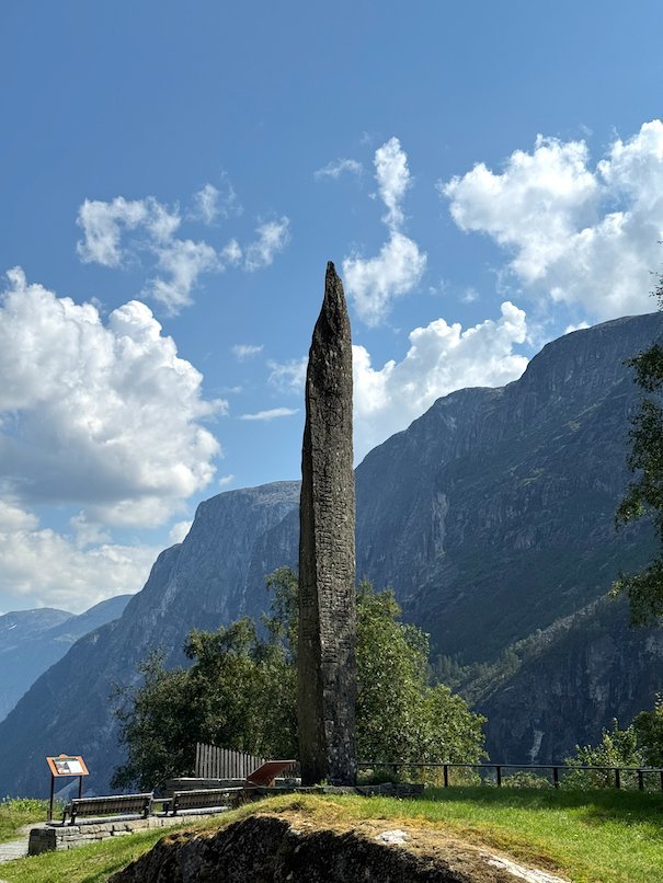 Tall stone pillar monument at Stalheim, with steep mountains and blue sky behind