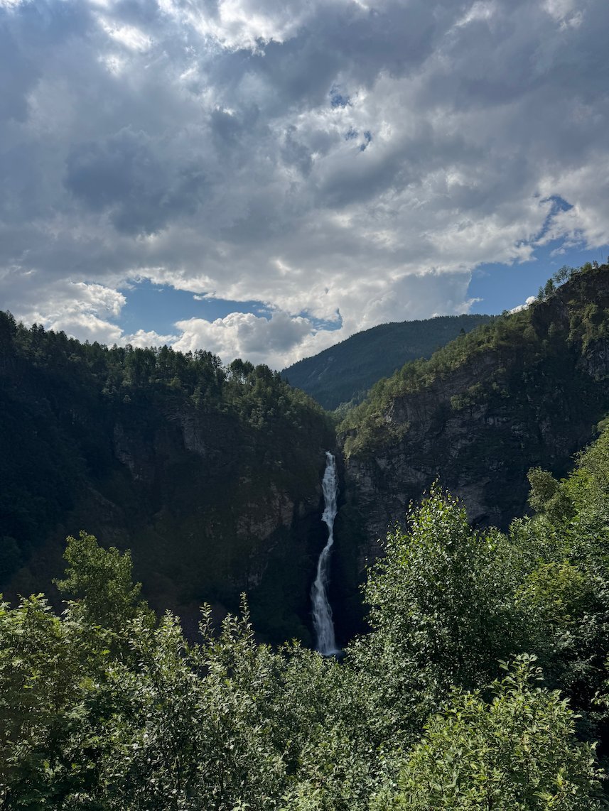 Waterfall in a narrow forested valley under grey and white clouds, near Stalheim