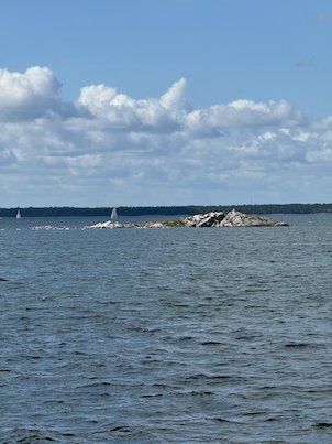 Small rocky skerry in open water under white clouds