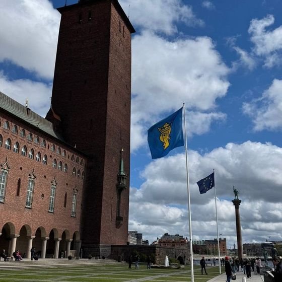 The tower of Stockholm City Hall against a blue sky, with the Swedish flag flying, photographed by Zayera Khan