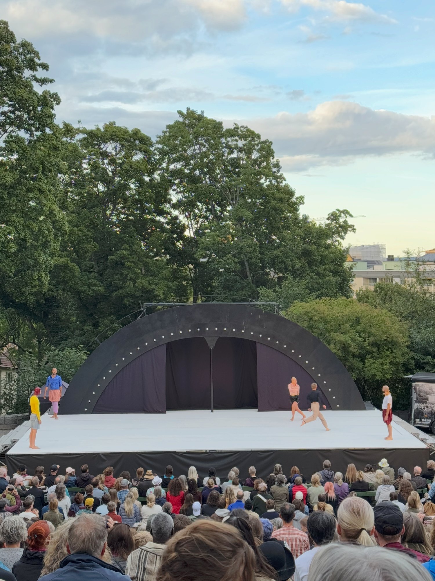 Dancers on an open-air stage in Stockholm, with a large audience in front and trees behind