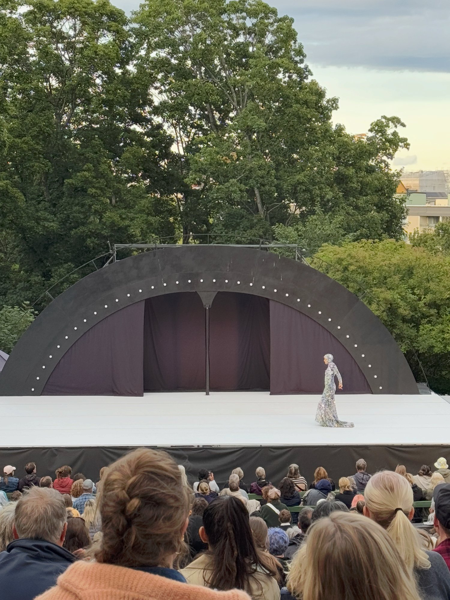 Solo dancer in a long dress on an open-air stage in Stockholm, seen over the heads of the audience