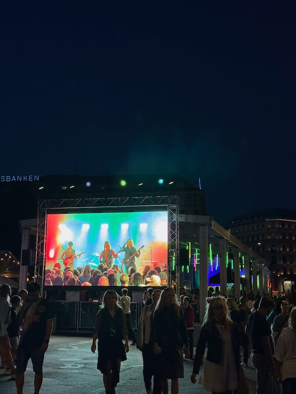 Crowd in front of an outdoor stage with a large screen at night in central Stockholm