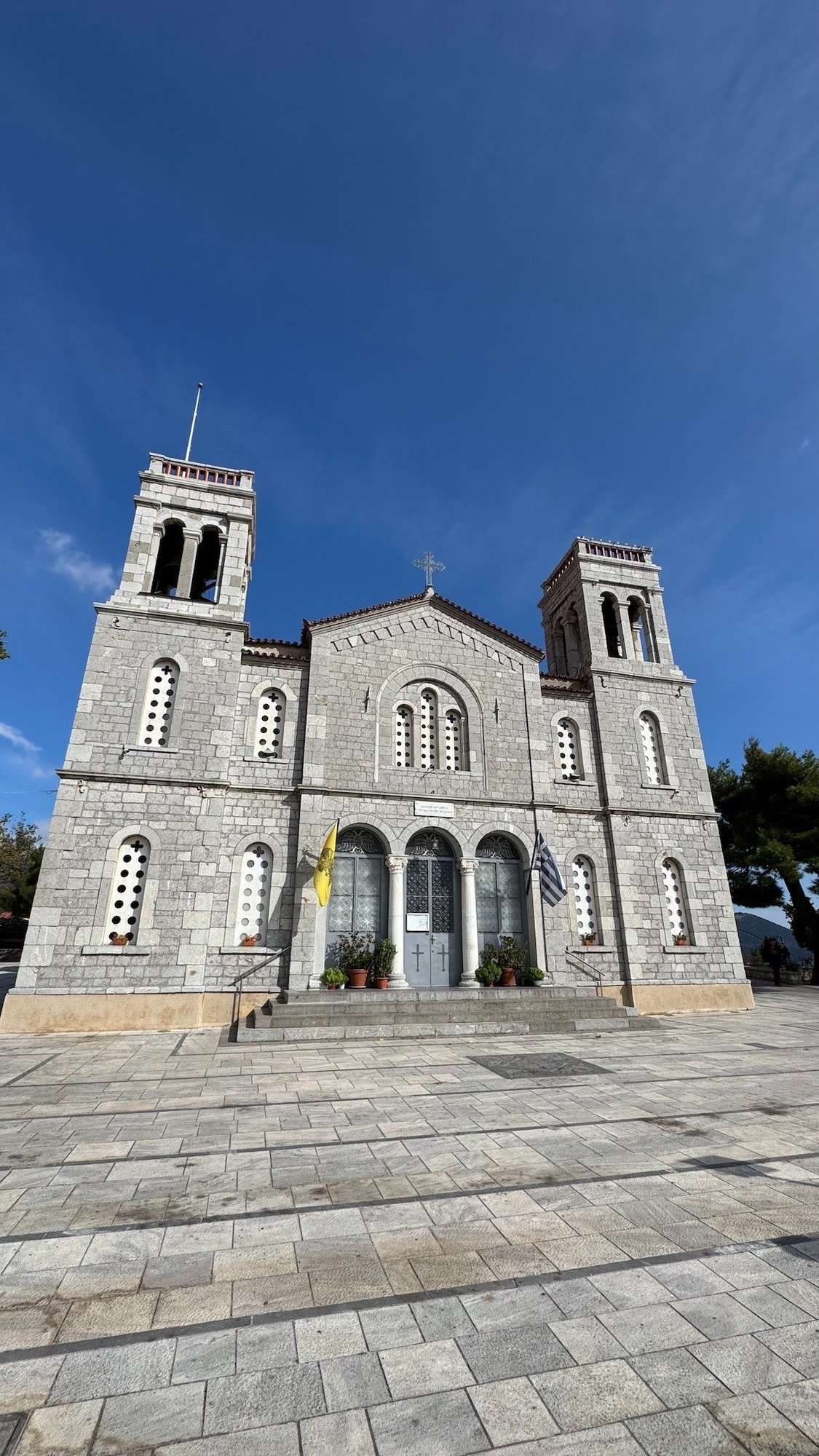 Stone church with two bell towers and a wide paved square in a mountain village near Delphi