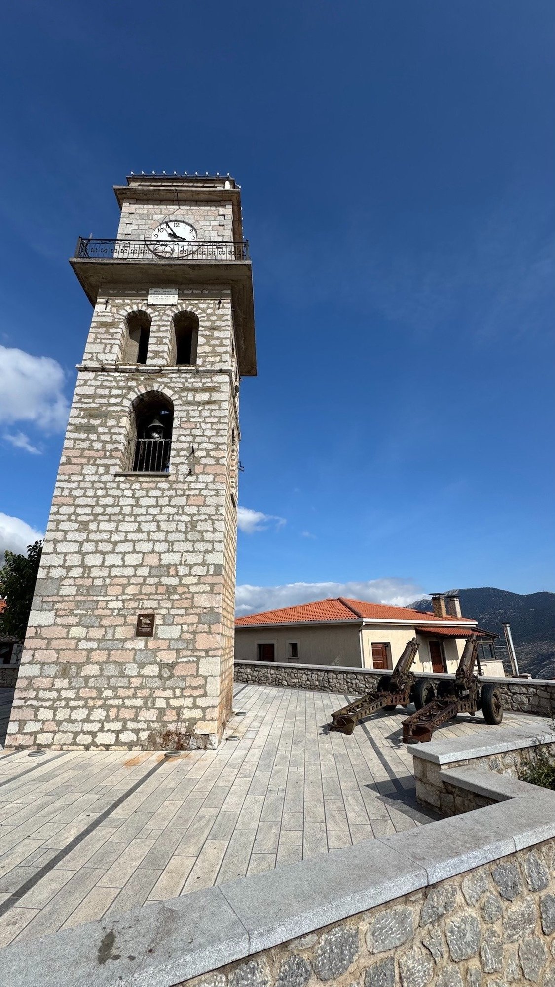 Stone clock tower on a paved square in a mountain village near Delphi