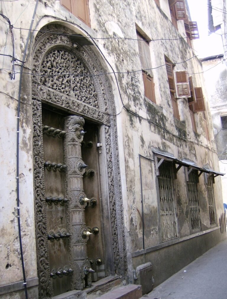 A tall carved wooden door with an arched top and brass studs stands in Stone Town, Zanzibar.