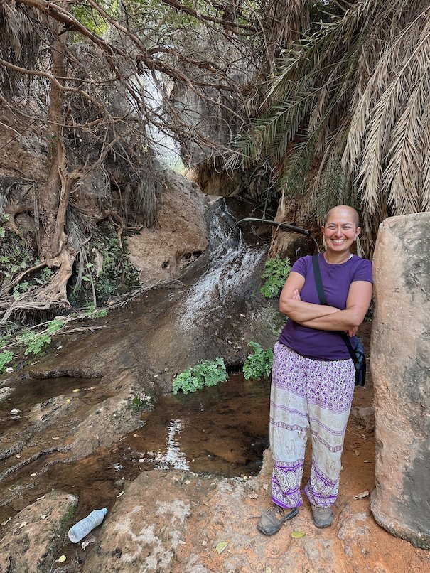 Zayera Khan stands with arms crossed next to a small waterfall in the Terjit oasis.