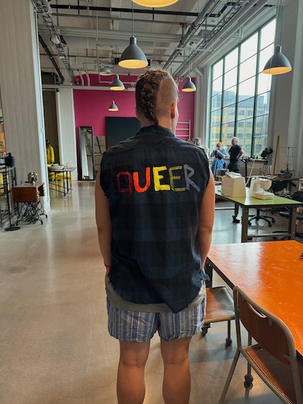 Person seen from behind in a vest with the word QUEER in coloured letters