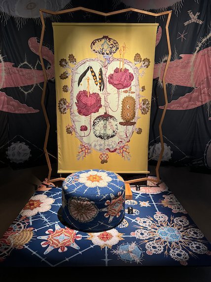 Embroidered textile artwork with flowers and a round cushion in front