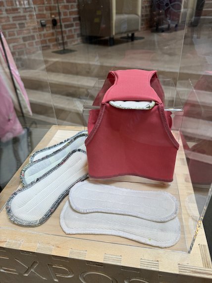 Red textile vest and washable pads in a glass case at the Textile Museum of Sweden