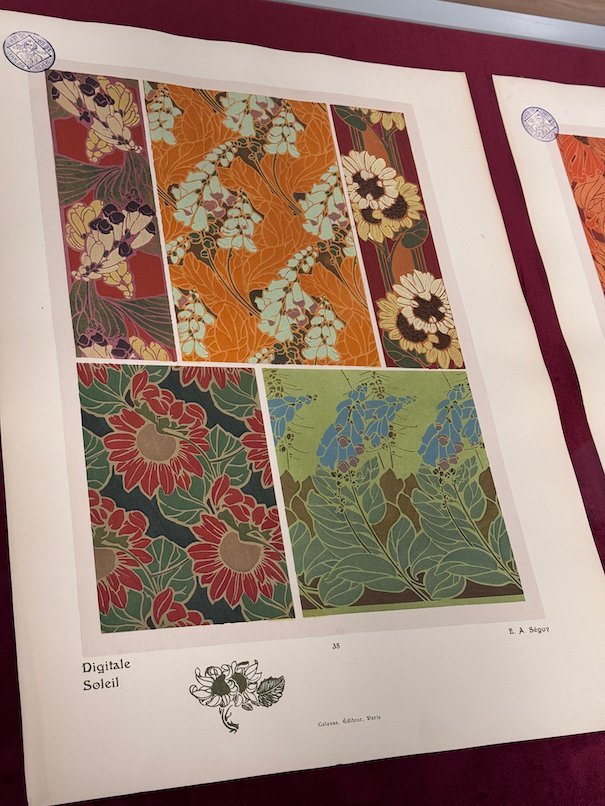 An Art Nouveau print with dahlia patterns in red and green hangs in Trier.