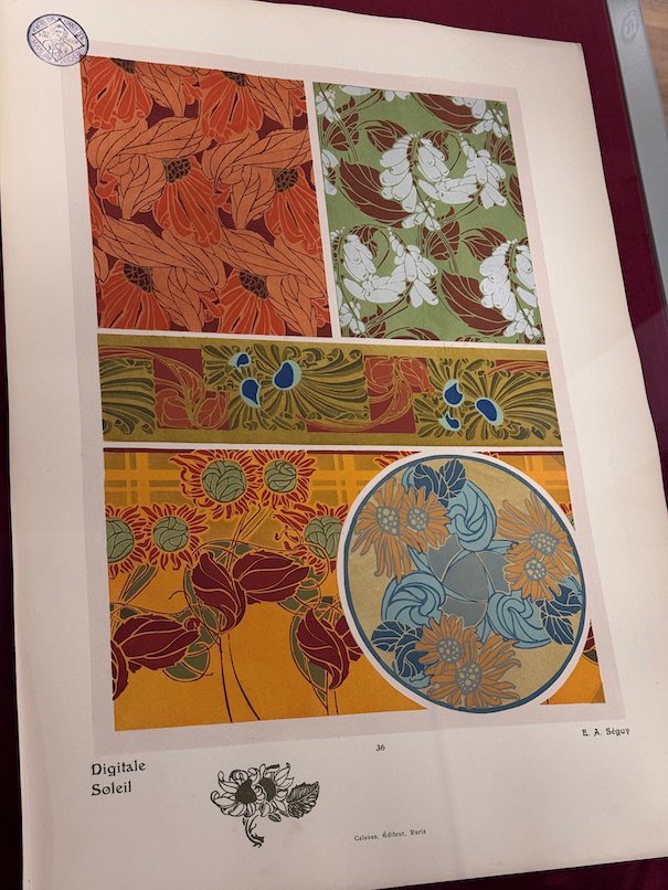An Art Nouveau print with orange flowers and a round pattern hangs in Trier.