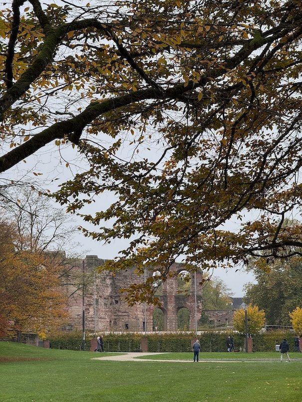 Roman ruins are visible through autumn trees across a park in Trier.