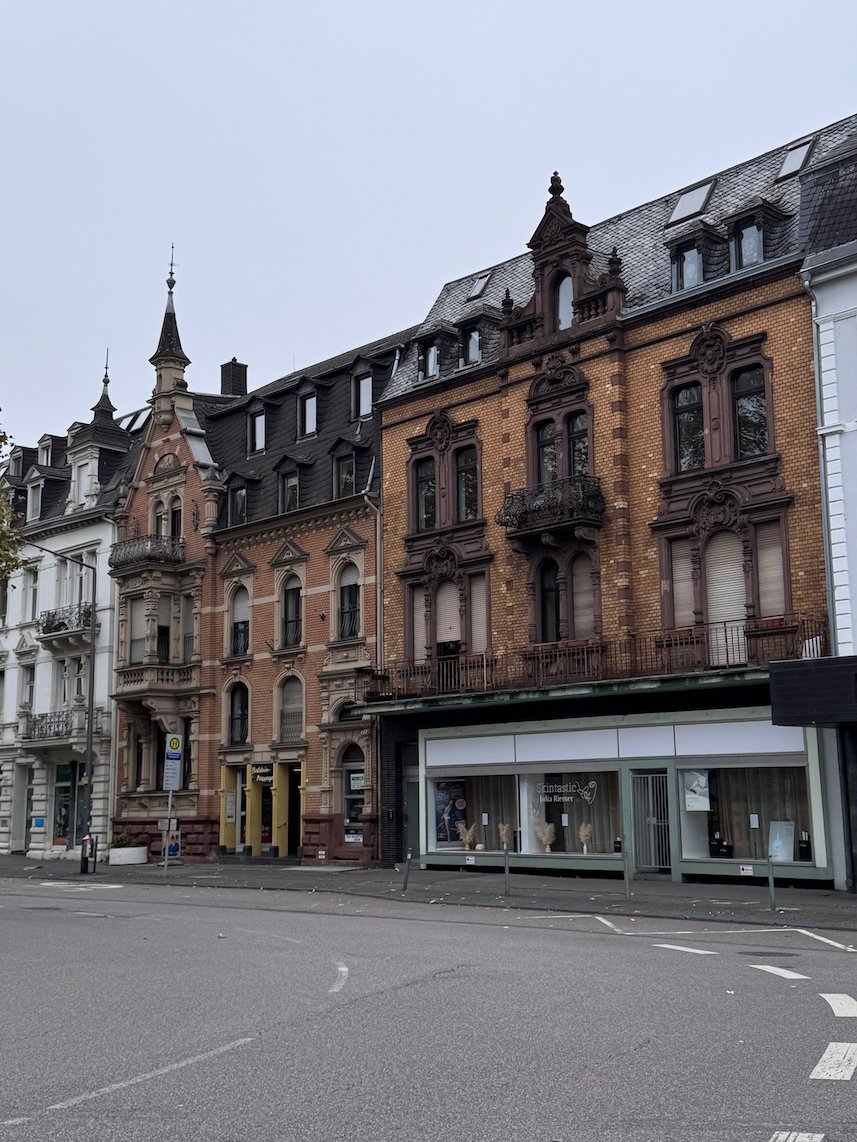 Old brick townhouses with small towers stand on a street corner in Trier.
