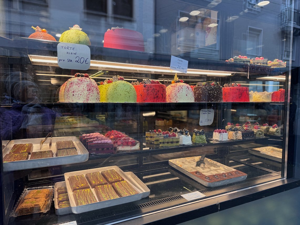 Colorful cakes and pastries fill the display window of a bakery in Trier.
