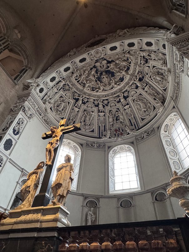 A golden crucifix stands under the white baroque apse of Trier Cathedral.