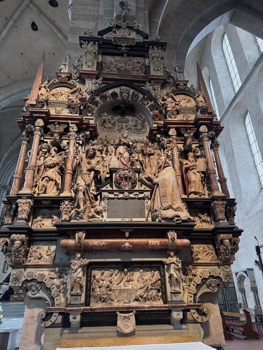 A tall carved stone altar with many figures stands in Trier Cathedral.