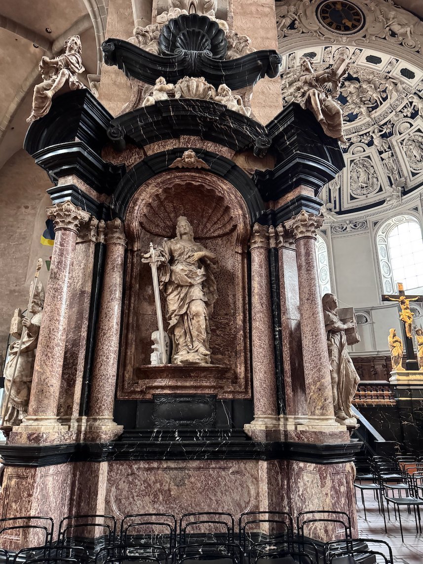 A statue stands in a marble altar with black columns in Trier Cathedral.