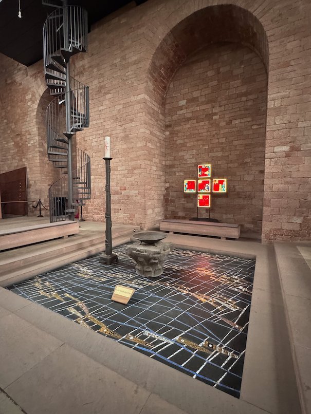 A red glass cross hangs above a simple altar in a brick chapel in Trier.