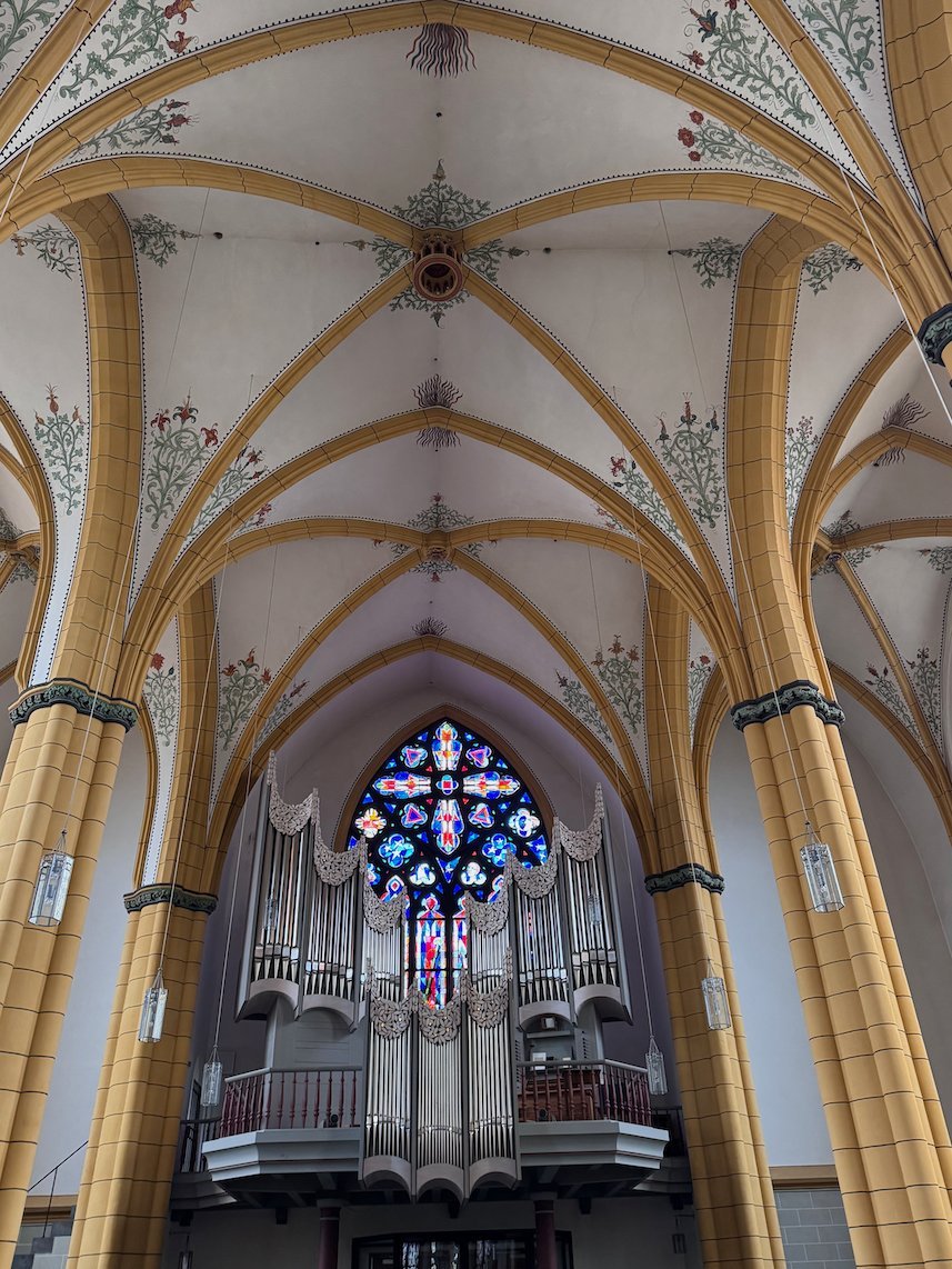 Yellow painted ribs of a vault lead to the organ in a church in Trier.