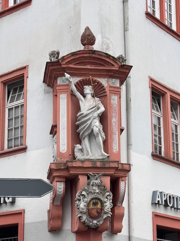 A white statue stands in a red niche on the corner of a house in Trier.