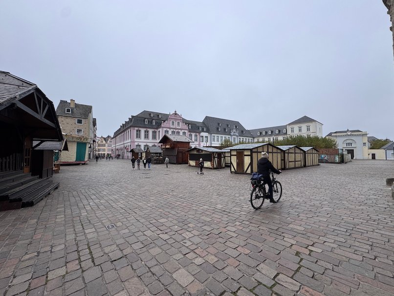 A cyclist crosses a wide cobbled square with market stalls in Trier.