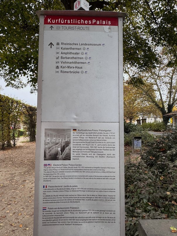 A signpost for the Electoral Palace stands next to a garden path in Trier.