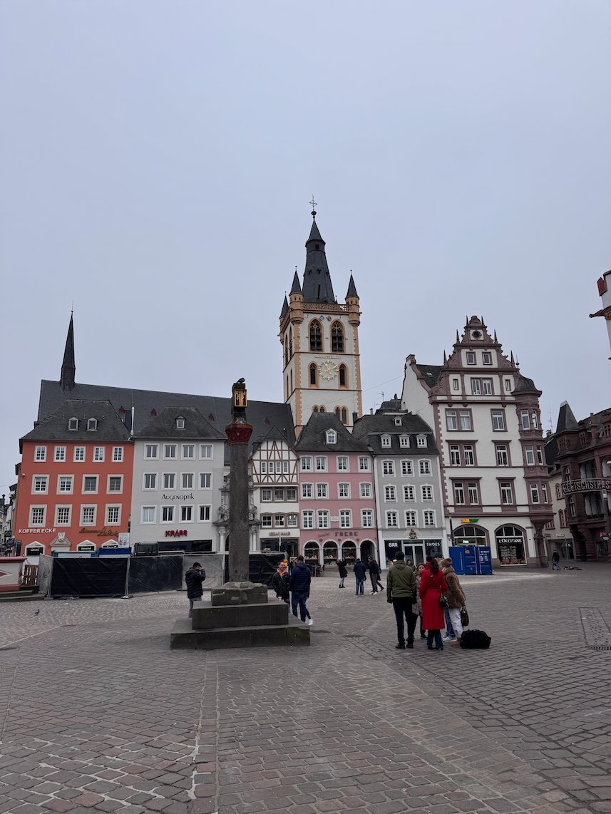 The tower of St. Gangolf rises behind the market cross on the Hauptmarkt in Trier.