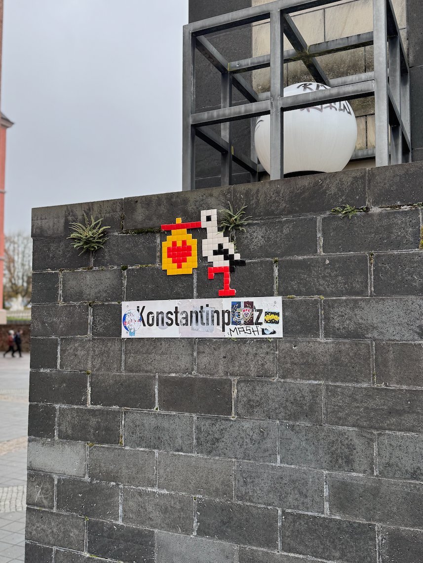 A street sign for Konstantinplatz hangs on a dark stone wall in Trier.